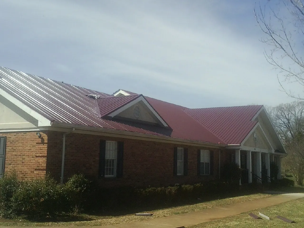 Red metal roof with gabled entries on a long brick building, from a Hail Damage Roof Repair job in Croydon